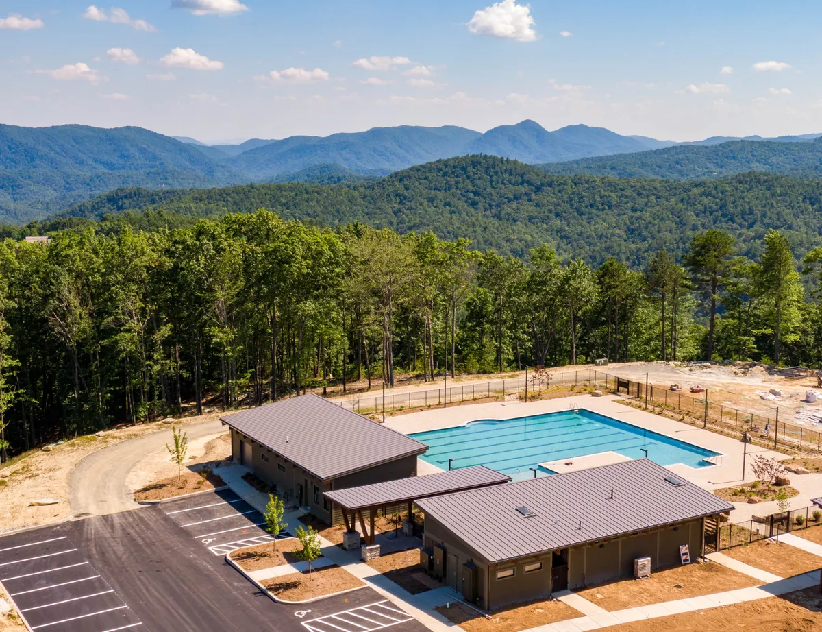 A sparkling swimming pool set against a backdrop of majestic mountains and a modern clubhouse, with plenty of space for sunbathing, relaxing, and social gatherings. Lounge chairs line the pool, inviting guests to unwind and take in the panoramic views.
