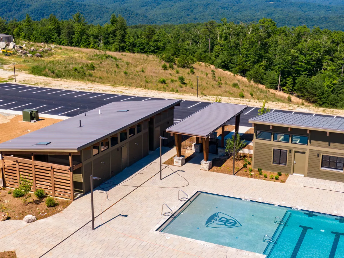 A vibrant scene featuring a large swimming pool, an outdoor shelter for shade and gatherings, lush landscaping, and a view of the surrounding area. The setting is inviting for both active and relaxing group activities.
