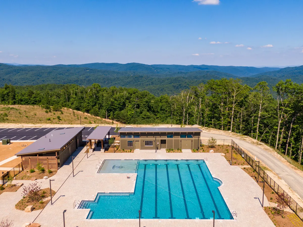 A lively outdoor pool scene with the poolside lounge area, majestic mountains in the background, and a visible community building. The space is designed for both recreation and social gatherings, embodying the communal spirit of the amenities on offer.