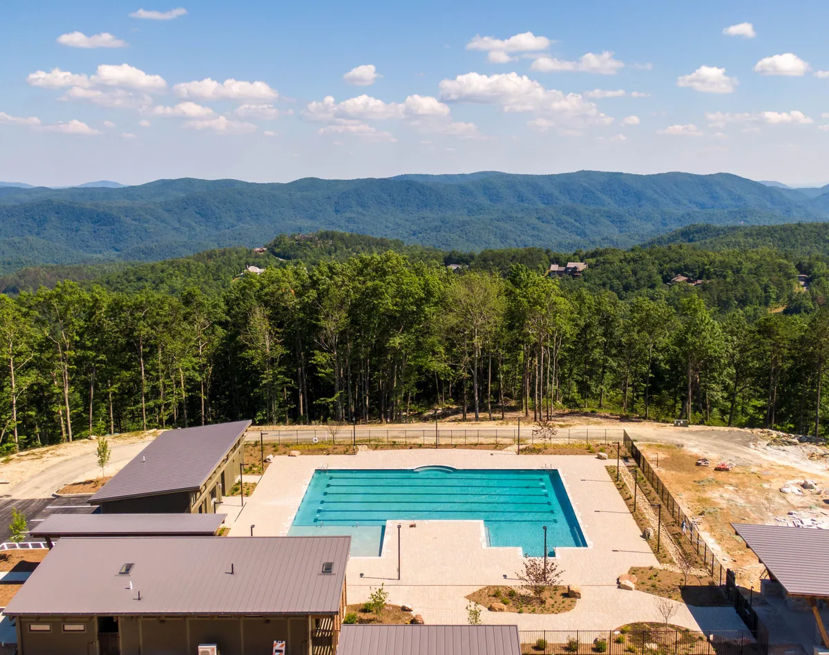 A serene exterior shot of the expansive outdoor swimming pool with stunning mountain views and lush forest surroundings. Modern buildings and lounging areas frame the pool, inviting guests to relax, swim, or join community events while soaking in the natural beauty.