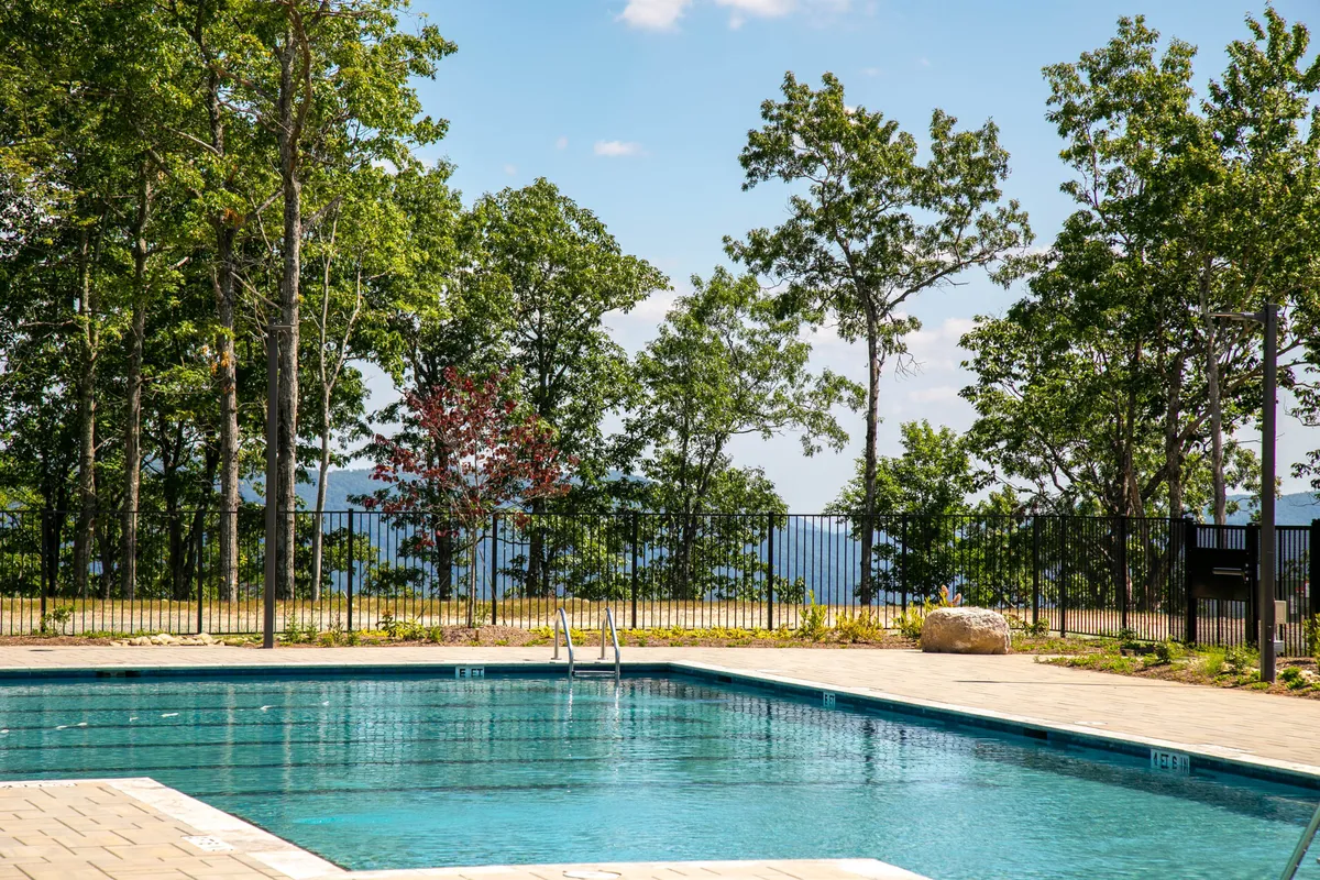 This image shows a serene swimming pool surrounded by trees and distant mountain views. The pool area is spacious and tranquil, providing a sense of the property's natural beauty and recreational options. While the pool itself is a seasonal amenity, the surrounding landscape hints at the miles of trails and open areas nearby.