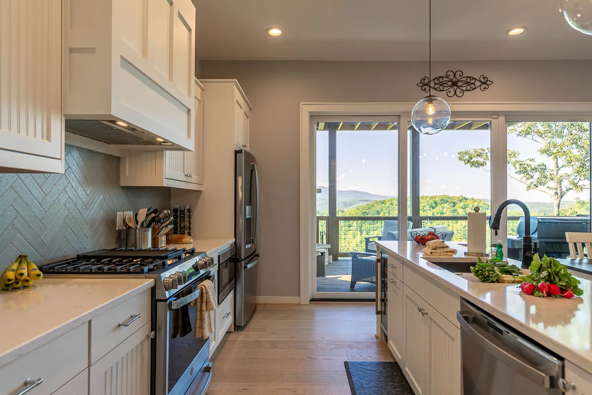 A chef’s kitchen with a spacious island, stainless steel appliances, and a clear view through the windows to the outdoors. The setting is ideal for cooking, entertaining, and bringing people together in a bright, inviting space.