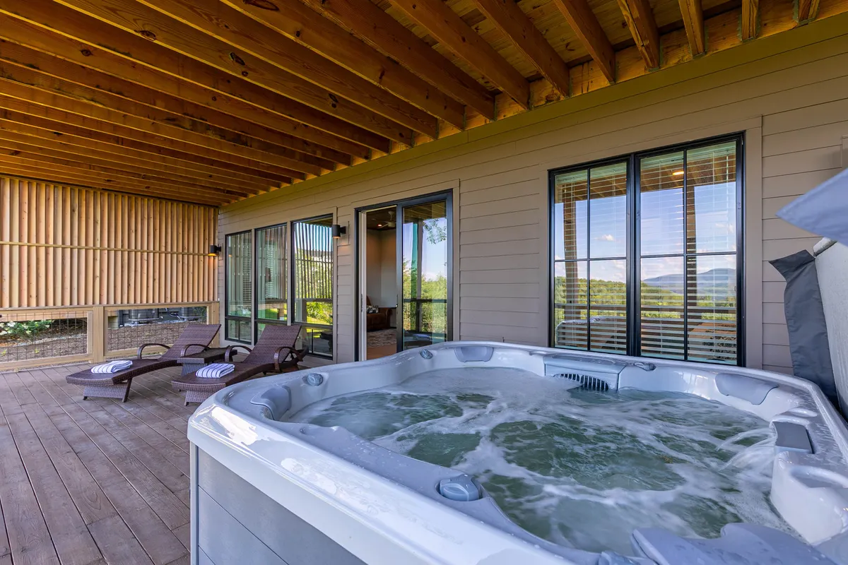 A tranquil deck area with a hot tub and comfortable chairs, overlooking the mountains and surrounded by nature. The setup invites relaxation and taking in the scenery after a day spent exploring.