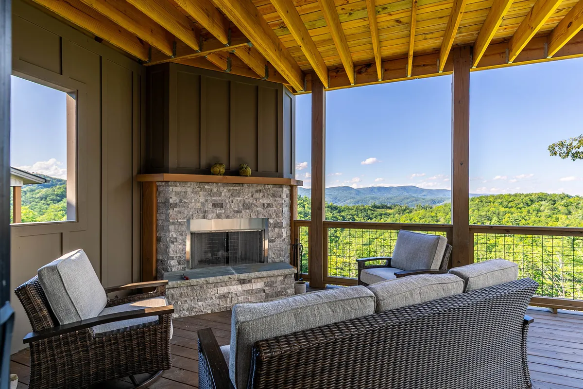 This image features an inviting exterior deck setting with a prominent fireplace, comfortable outdoor lounge seating, and panoramic mountain views. The sun is setting, creating a warm glow and tranquil atmosphere perfect for evening relaxation.