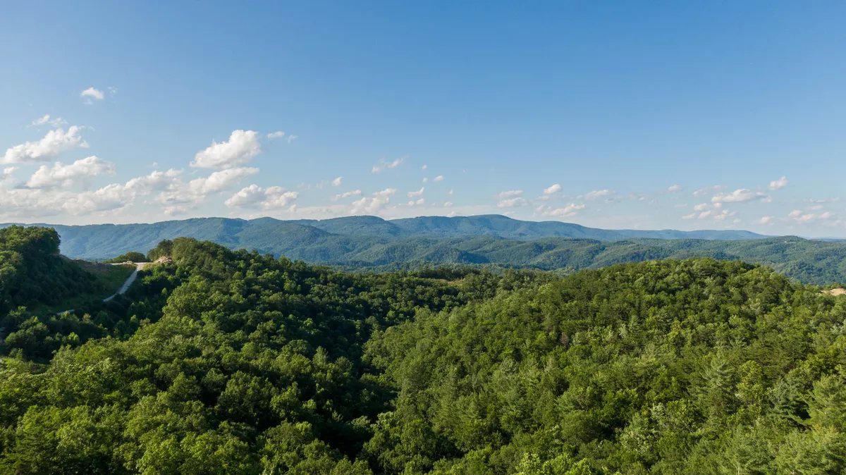 A breathtaking panoramic view of rolling hills, distant Blue Ridge Mountains, and lush greenery. The setting is open and natural, with wide skies and forests that hint at endless trails to explore. The sense of scale and wilderness evokes the spirit of adventure and the beauty of untouched nature.