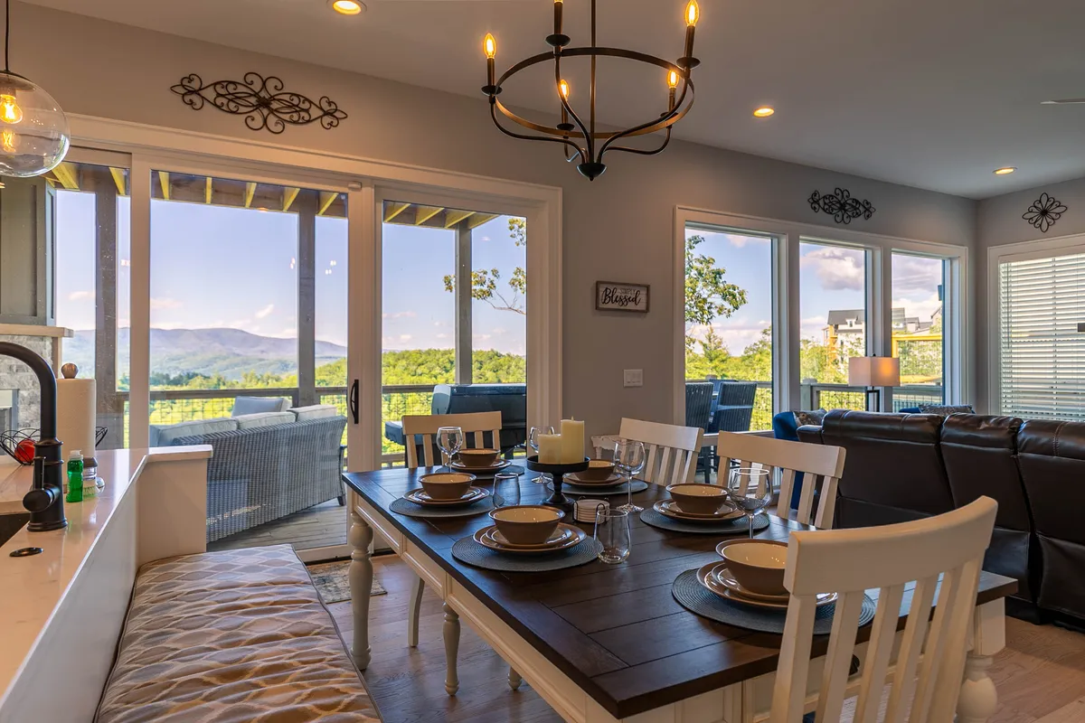 A warm and welcoming dining area with a table set for a meal positioned near expansive windows that look out onto the mountains. A stylish chandelier adds ambiance, and the layout invites communal gatherings and memorable meals.