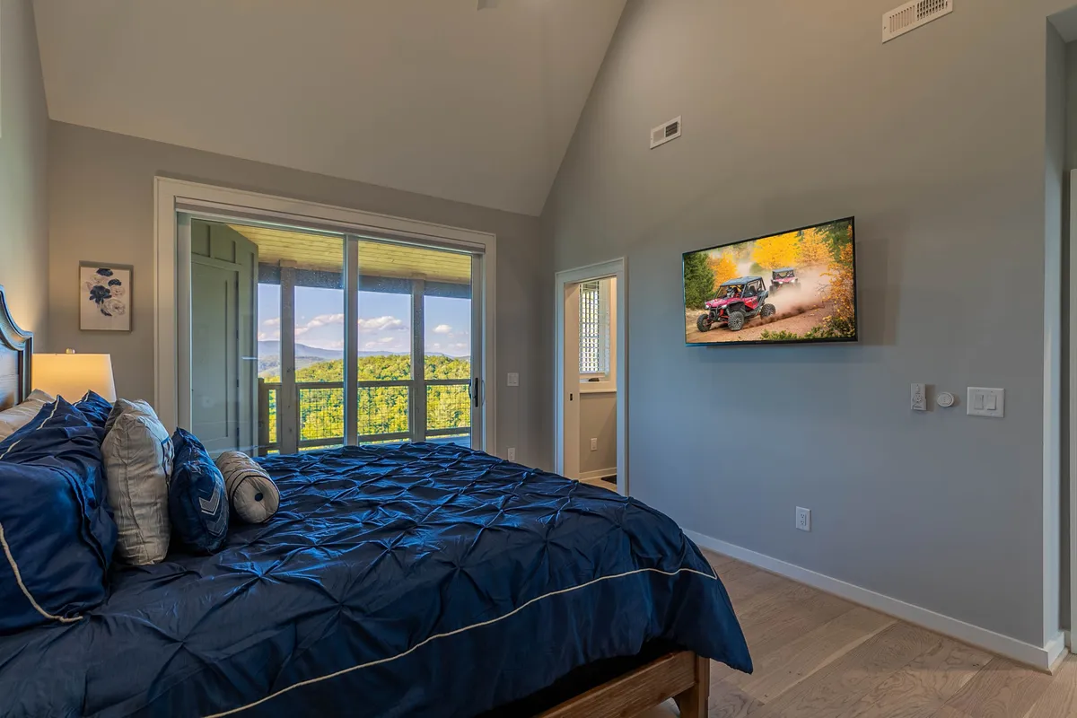 This image features a king bedroom with blue bedding, large windows that frame a stunning mountain view, and a TV mounted on the wall. The space exudes comfort and tranquility, with soft natural light filling the room and inviting guests to relax in plush surroundings.
