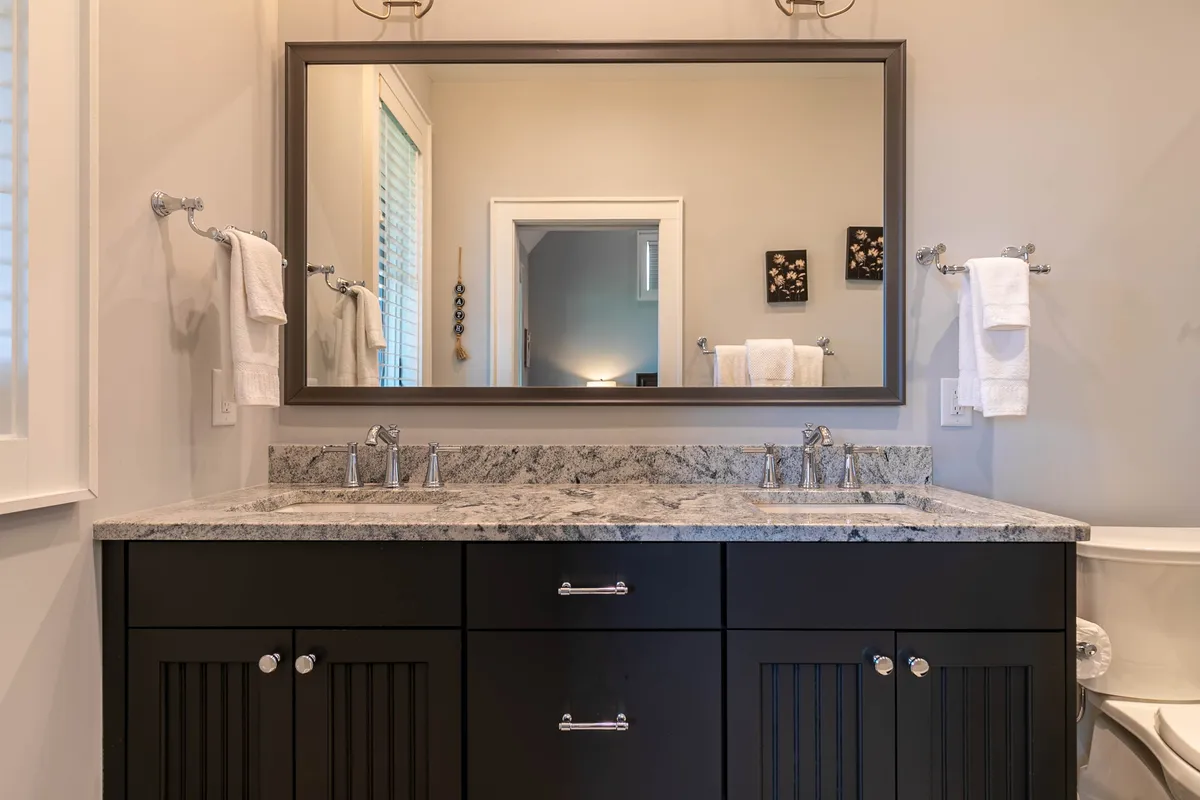 A modern en suite bathroom with a double sink granite countertop, large mirror, and sophisticated fixtures. The clean lines and soothing tones create a spa-like environment, perfect for morning routines or unwinding after a day of adventure.
