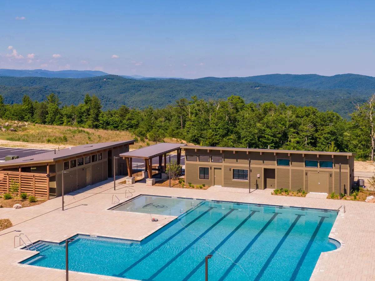 A serene swimming pool lies at the center, surrounded by comfortable cabanas and lush landscaping, with the majestic Blue Ridge Mountains rising in the background. The atmosphere is relaxed, inviting, and perfect for family enjoyment.