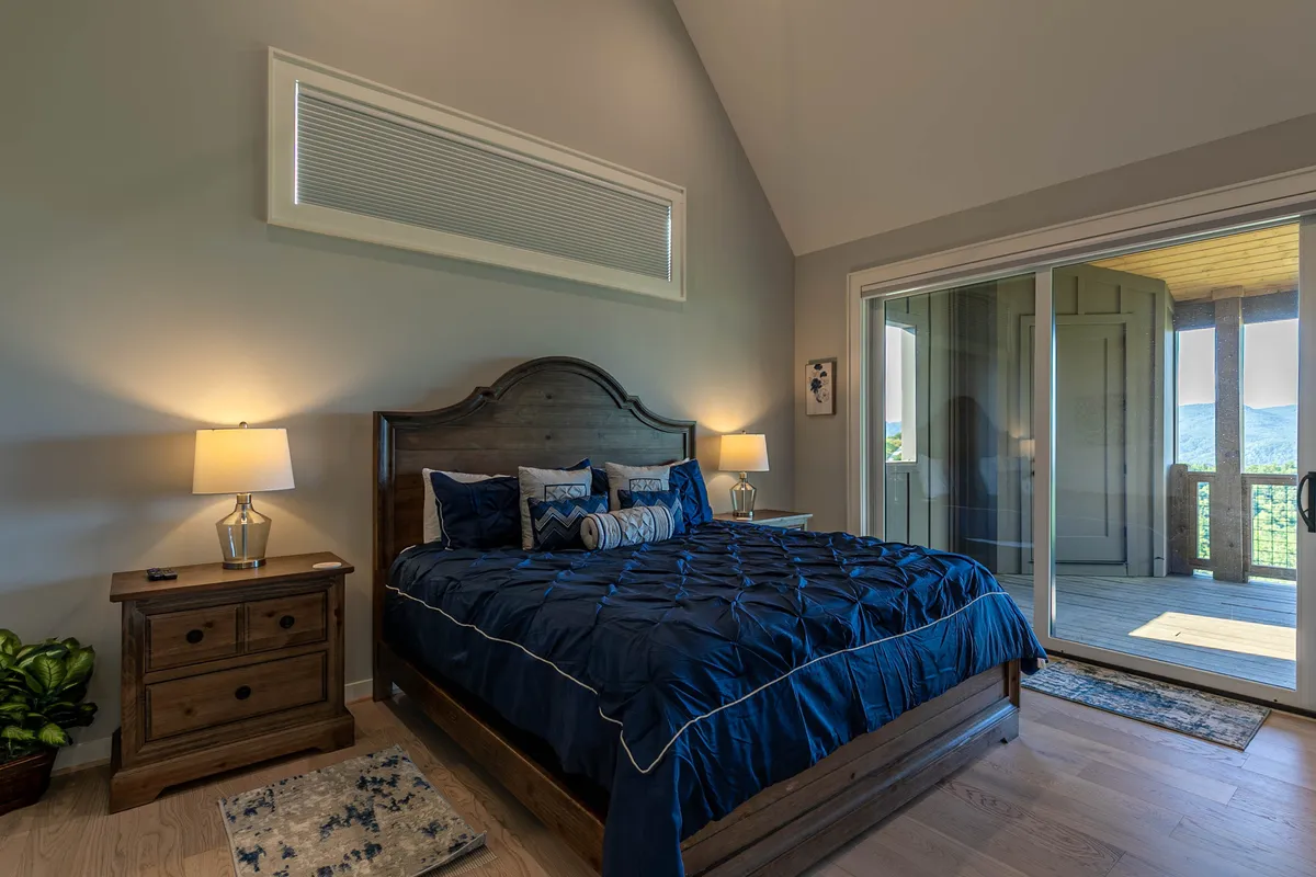 A serene king bedroom with a comfortable bed, nightstand, and sliding glass door that opens to a scenic view. The space is designed for relaxation, with minimalist decor that emphasizes the peaceful connection to nature just beyond the window.