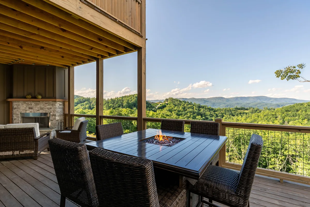 An inviting exterior space featuring an outdoor dining table set, a cozy fire pit, and sweeping mountain views. The warm, communal setting suggests moments of relaxation and socializing after a day spent outdoors.