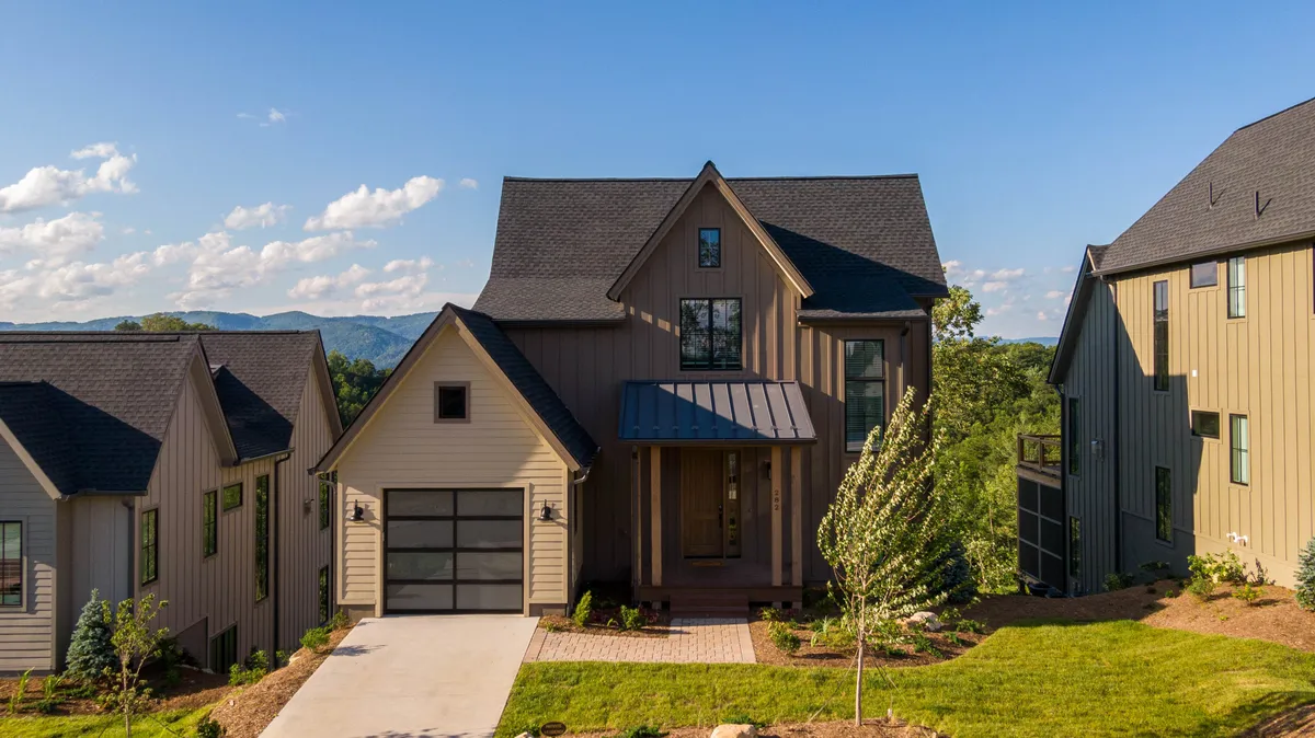 This exterior shot features a welcoming front porch with large windows, a landscaped yard, and a driveway. The scene is open and inviting, suggesting ample space for outdoor activities and relaxation. The porch overlooks both the yard and the natural surroundings, making it an ideal spot for enjoying the outdoors with pets.