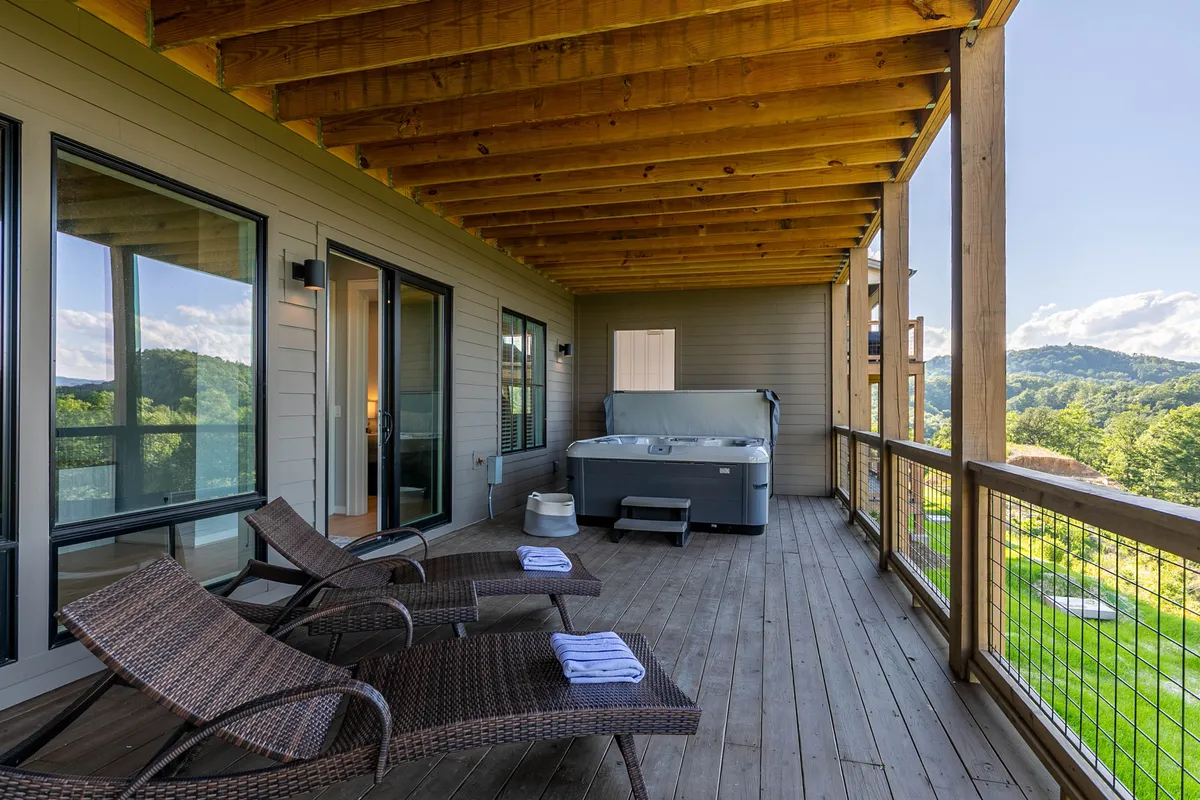 A secluded lower deck features a bubbling hot tub flanked by reclining chairs, all oriented to maximize the peaceful mountain view. The setting feels private and tranquil, inviting relaxation in nature.