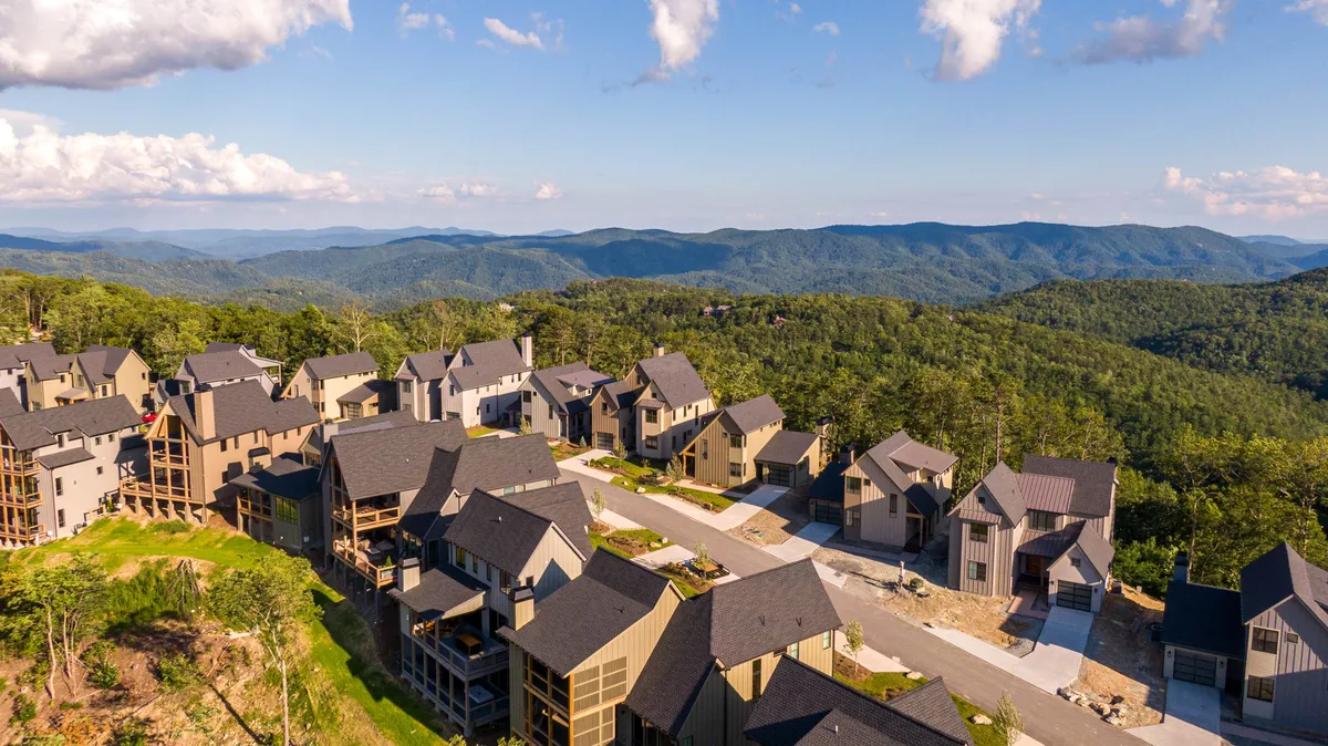 A row of modern homes lines a winding road, stretching out towards expansive, layered mountain vistas beneath an open sky. The scene captures the community’s setting and the sense of arrival to a vibrant, adventure-filled mountain retreat.